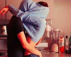 a woman sitting on top of a kitchen counter covered in a blue blanket over her head