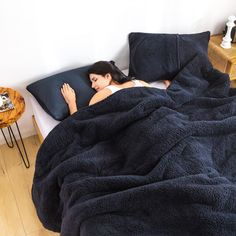 a woman laying in bed under a blue blanket