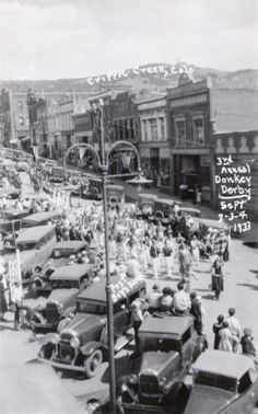 an old black and white photo of many cars in the street with people standing around