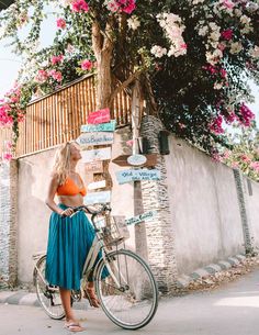 a woman standing next to a bike in front of a wall with flowers on it