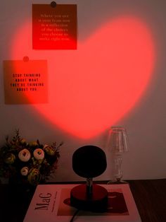 a heart shaped object sitting on top of a table next to a vase with flowers