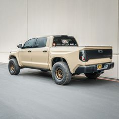 a tan truck parked in front of a white wall with orange stripes on it's sides