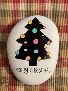 a painted rock with a christmas tree on it sitting on a plaid tablecloth covered surface