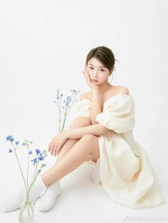 a woman sitting on the ground next to some blue flowers in a vase with her legs crossed