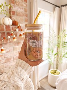 a person holding a jar with a straw in it next to a brick wall and potted plant