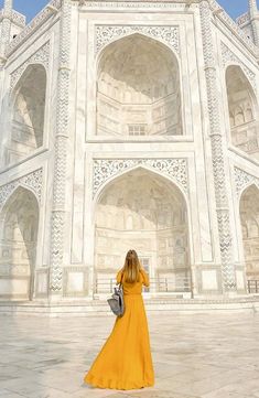 a woman in a yellow dress standing in front of a white building with arches and pillars