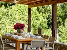 a wooden table with white chairs under a pergolated roof and trees in the background