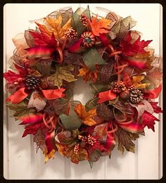 a wreath with autumn leaves and pine cones hanging on a front door or entryway