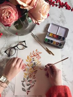 a woman is painting flowers with watercolors on paper