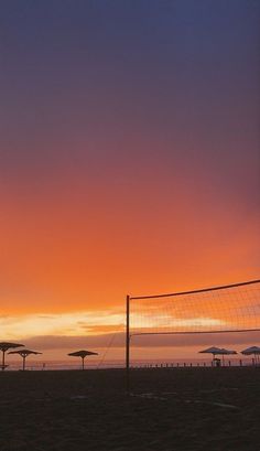 the sun is setting at the beach with umbrellas and volleyball nets in the foreground