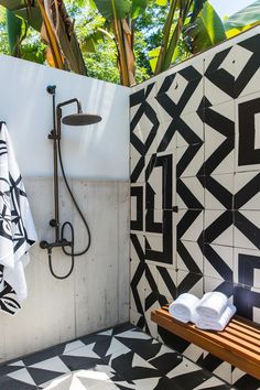 a bathroom with black and white tiles on the wall, shower head, and wooden bench