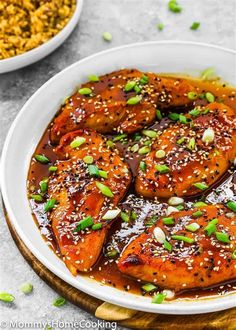 a white plate topped with chicken covered in sesame seeds and sauce next to a bowl of rice