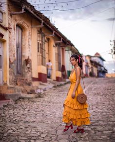 a woman in a yellow dress is standing on the cobblestone street with her handbag