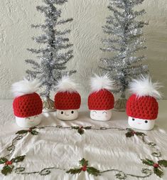 three crocheted santa hats sitting on top of a bed next to christmas trees