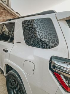 a white suv parked in front of a brick building with leopard print on the window