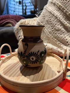 a brown vase sitting on top of a wooden tray next to a white and black blanket