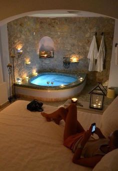 a person laying on a bed in front of a jacuzzi tub with candles