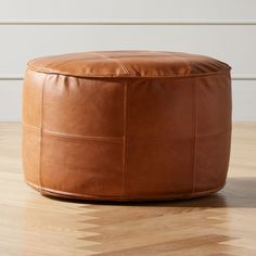 a brown leather ottoman sitting on top of a hard wood floor next to a white wall