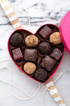 a heart shaped box filled with chocolates on top of a marble table next to a pink container