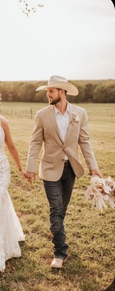 a bride and groom holding hands walking through a field