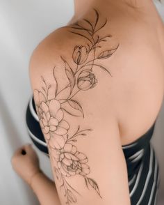 the back of a woman's shoulder with flowers and leaves tattoo on her arm