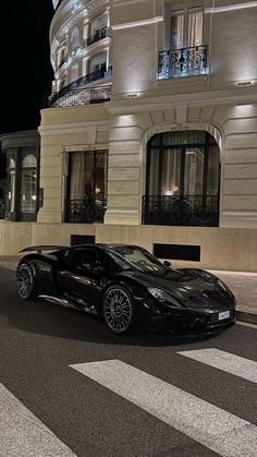 a black sports car is parked in front of a building at night with its lights on