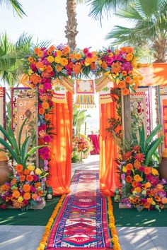 an orange and pink wedding arch with flowers on the side is surrounded by palm trees