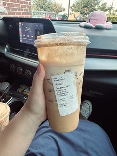 a person holding up a cup of coffee in their hand while sitting in the driver's seat of a car