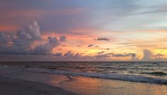 the sun is setting over the ocean with clouds in the sky and waves on the beach