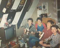 four young men sitting in a living room with guitars on the floor and one holding a guitar