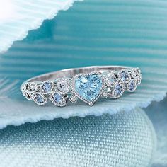 a blue heart shaped diamond ring on top of a piece of cloth with diamonds around it