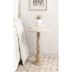 a small white table with a vase on top of it next to a bed in a bedroom