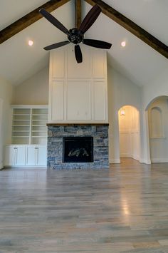 an empty living room with a fireplace and ceiling fan in the middle of the room