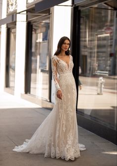 a woman in a wedding dress is standing on the sidewalk near a storefront and looking off into the distance