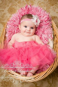 a baby wearing a pink dress sitting in a basket