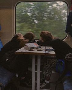 two people sitting at a table on a train looking out the window with trees in the background