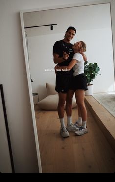 two people standing in front of a mirror with their arms around each other and smiling