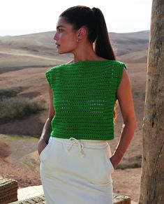 a woman wearing a green crochet top and white skirt