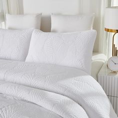 a bed with white comforters and pillows in a bedroom next to a clock on the wall