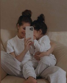 a woman holding a baby taking a selfie with her cell phone while sitting on a couch