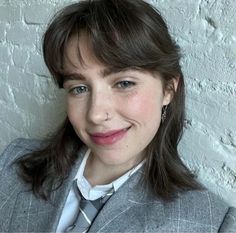 a woman wearing a suit and tie posing for a photo in front of a white wall