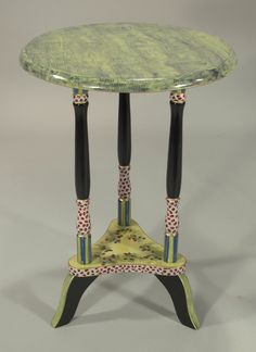 a green table with two black legs and a flowered design on the top, sitting against a gray background