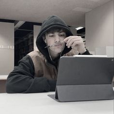 a man sitting at a table with a laptop computer in front of him and wearing a hoodie