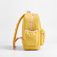 A backpack that's extra comfy and ready to handle all the adventures of the day. A pattern of quilted blooms add sunny vibes to the bag's yellow exterior, and contrasting pink trim gives it the perfect finish. Constructed of supremely durable polyester fabric that includes recycled plastic bottles, this medium knapsack's roomy interior holds everything your kid needs-books, school supplies, extra layers-and there's a padded pocket to keep their tablet protected. Outside pockets hold snacks, wate Cute Yellow Backpack For Students, Cute Yellow School Backpack, Cute Yellow Backpack For Back To School, Yellow Student Backpack For Back To School, Quilted Backpack For Back To School, Playful Yellow Bags For Back To School, Playful Yellow Backpack For Back To School, Quilted Standard Backpack For Back To School, Back To School Quilted Backpack