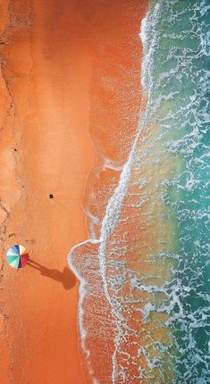 an aerial view of the beach and ocean with two people holding umbrellas looking out at the water