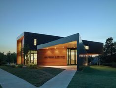 a modern building with wood and glass on the front entrance at night time, lit up by lights