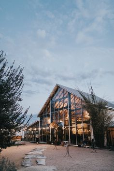 a large glass building sitting on top of a dirt field next to a green tree