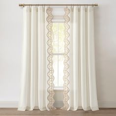 a white curtain with gold lace trim hanging on a window sill next to a wooden floor