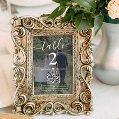 a table number frame with a wedding photo on it and flowers in the vase behind it