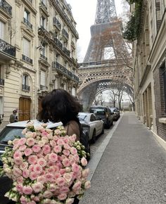 a woman is holding flowers in front of the eiffel tower, with cars parked near her